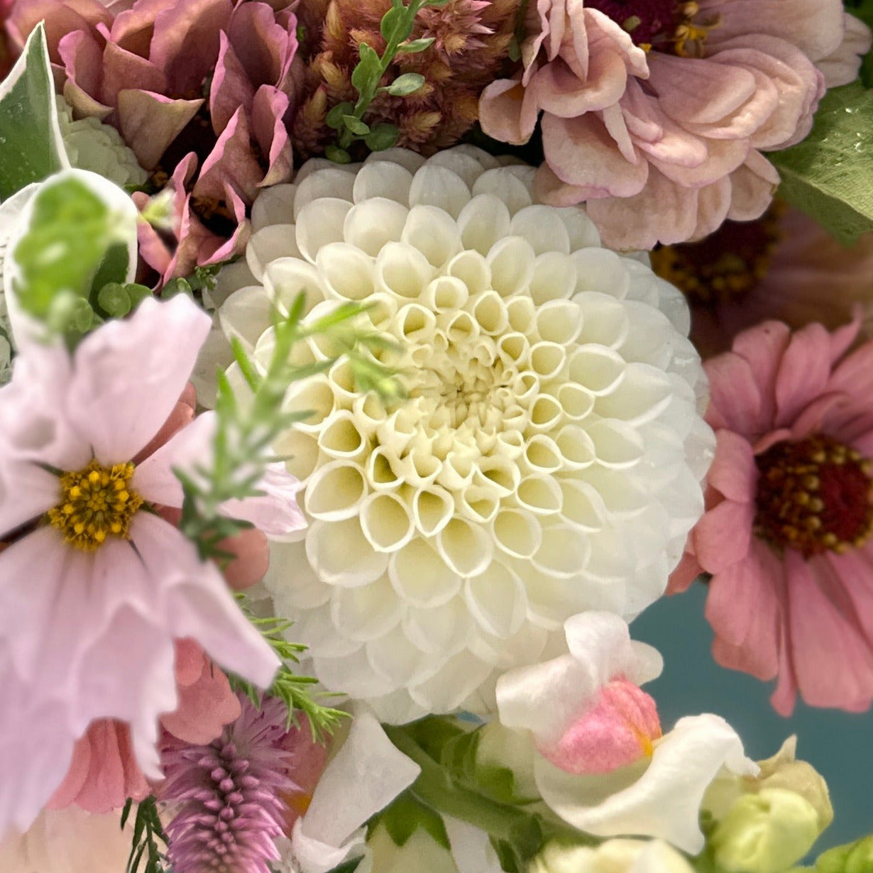 A close-up of a bouquet with a prominent white floral arrangement surrounded by pink and green flowers.