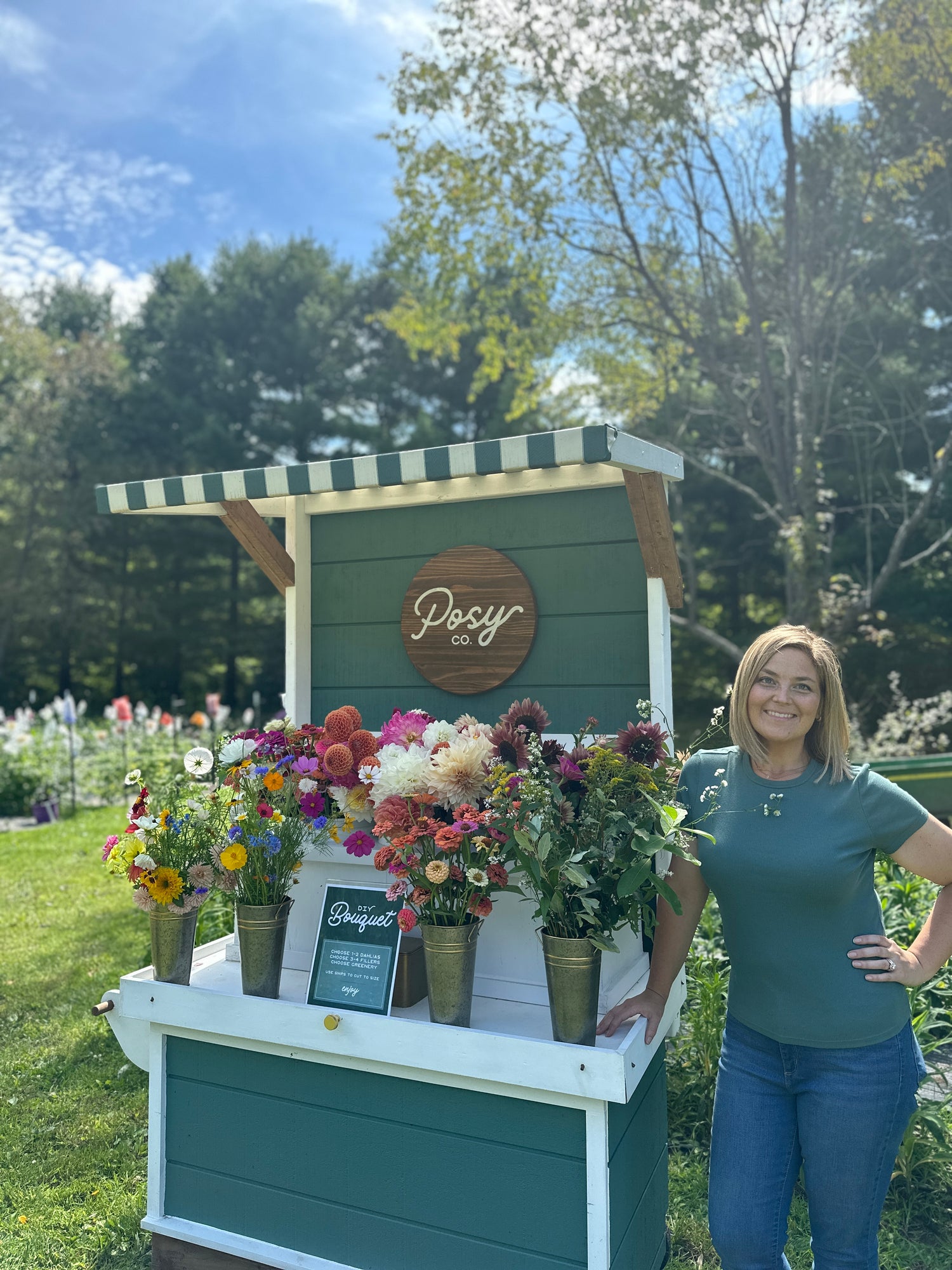 A flower stand with bouquets and a woman, the owner of Posy Co.